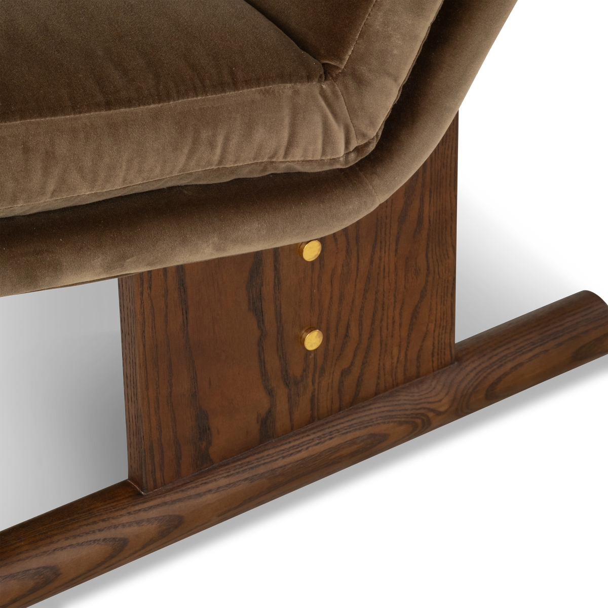 Close-up showing the Wallace Lounge Chair’s walnut-finished ash post with open grain and two brass-toned discs, below the folded edge of the Olive Brown velvet seat.
