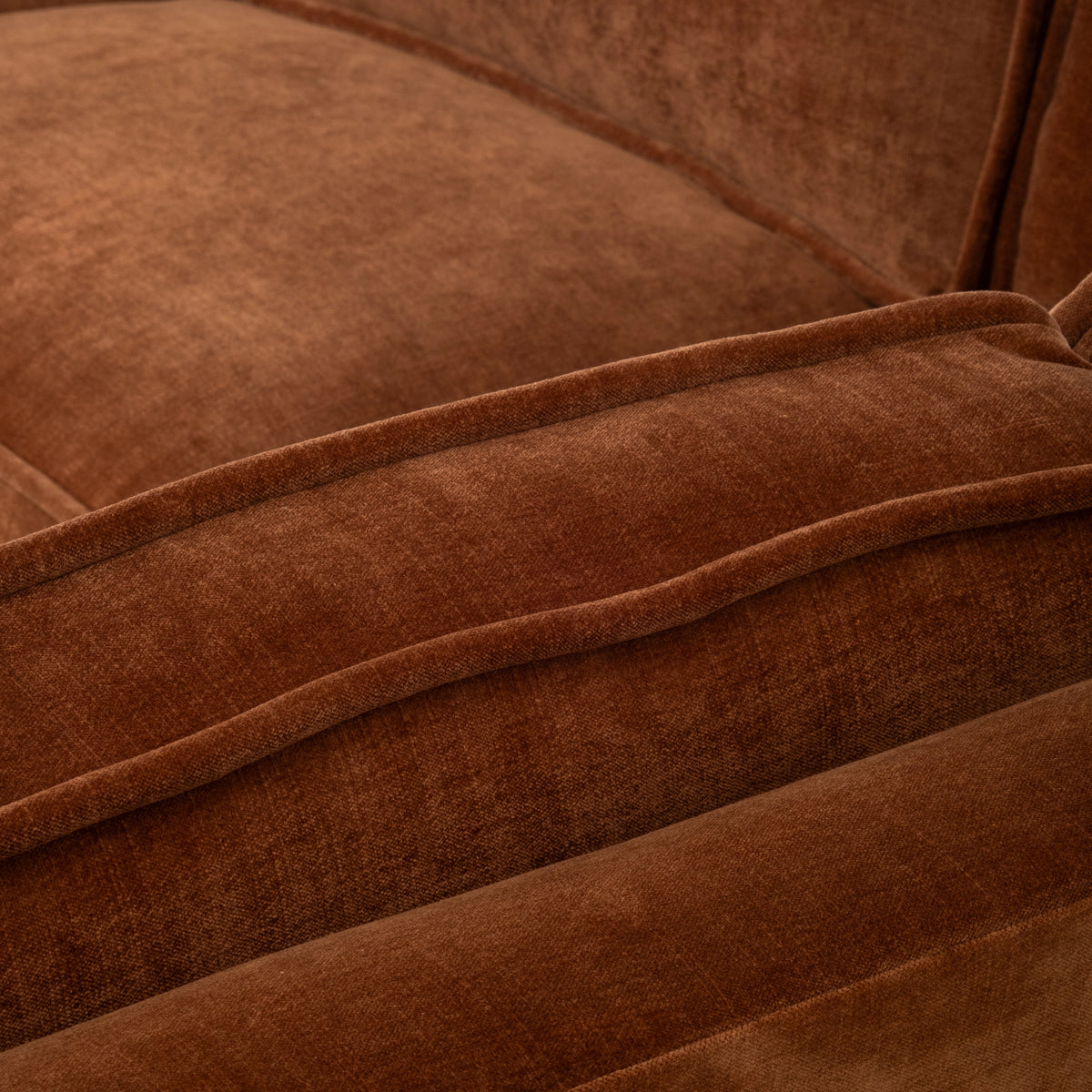 Detail shot of the Loom Modular Sectional in rust chenille, with the plush seat cushion, the double-piped front edge, and the back cushion above.