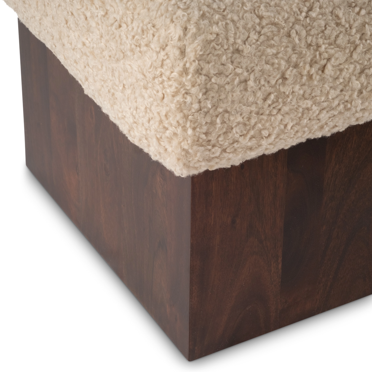 Close-up showing the Ciro Ottoman’s dark brown mango wood corner with rich reddish grain, beneath the edge of the cream faux shearling cushion.