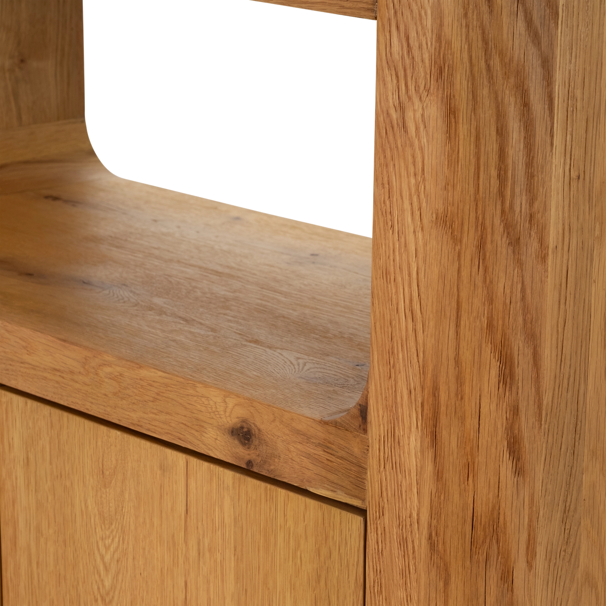 Edge Cabinet shown in close-up in honey oak, with a curved cove shelf where it meets the thick side panel and a prominent knot in the grain.