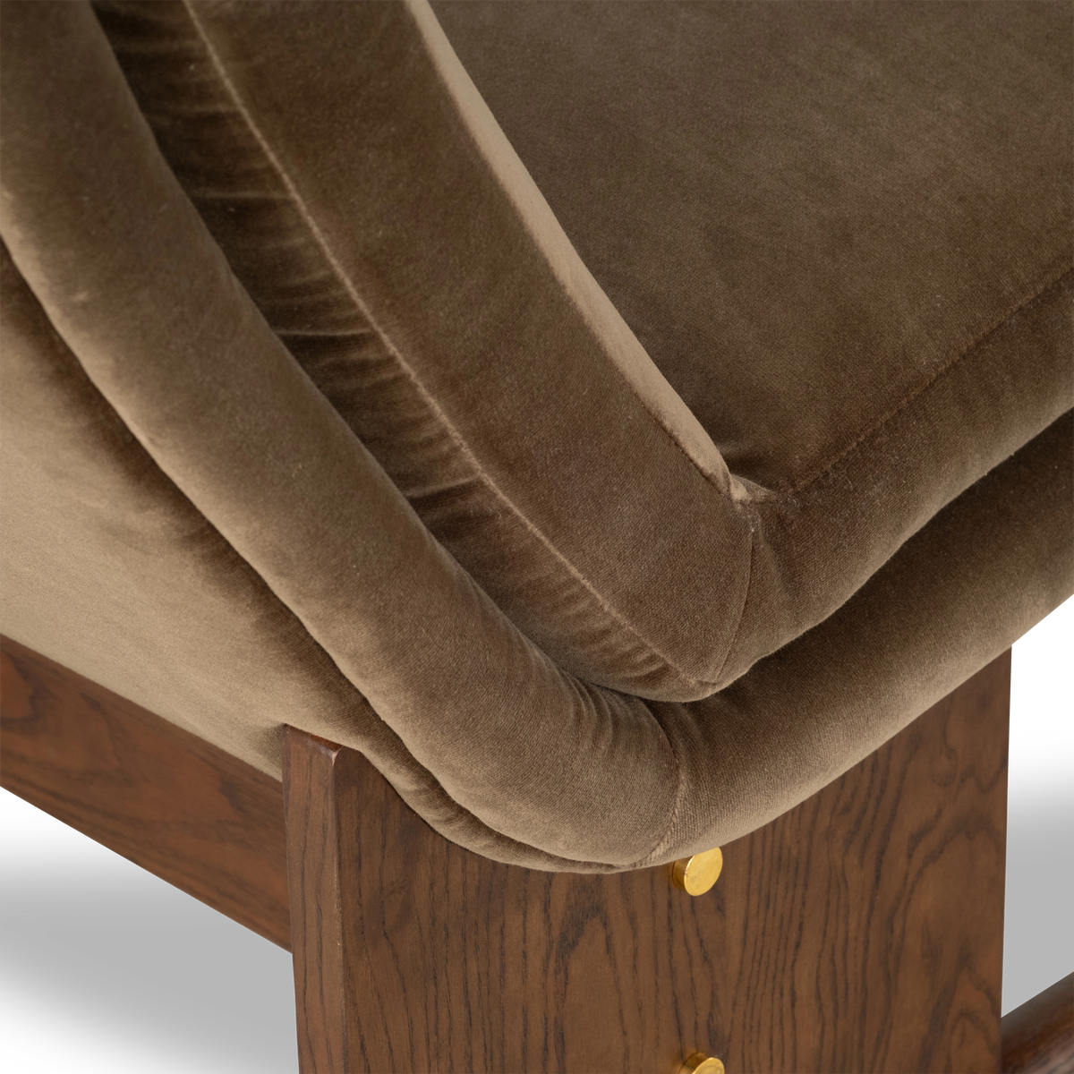 Close-up showing the Wallace Lounge Chair’s Olive Brown velvet seat edge and back shell with a stitched seam, resting on a walnut-finished ash post with a brass-toned disc.
